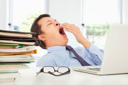 Exhausted young businessman yawning at work in office