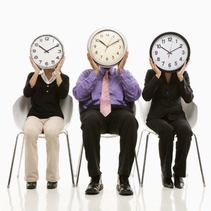 Multi-ethnic business people sitting holding clocks over faces.